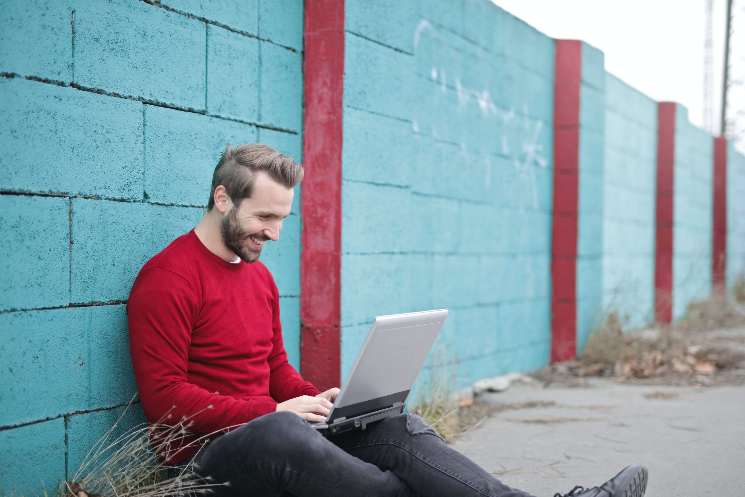 man-sitting-beside-wall-looking-at-laptop